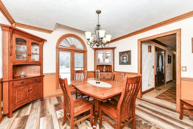 dining space featuring a textured ceiling, ornamental molding, a notable chandelier, and light wood-type flooring