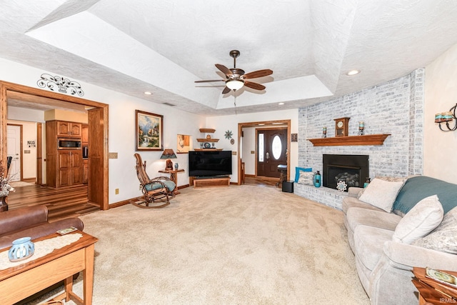 carpeted living room with a tray ceiling, ceiling fan, a fireplace, and a textured ceiling