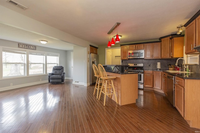 kitchen with stainless steel appliances, dark wood-type flooring, sink, a kitchen island, and a breakfast bar area