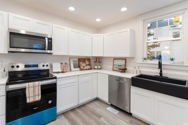 kitchen with white cabinetry, sink, light wood-type flooring, and appliances with stainless steel finishes