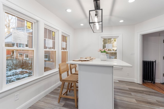 kitchen featuring radiator heating unit, a breakfast bar area, hanging light fixtures, and light hardwood / wood-style flooring