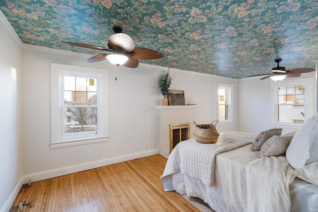 unfurnished bedroom featuring light wood-type flooring, a brick fireplace, ceiling fan, and ornamental molding