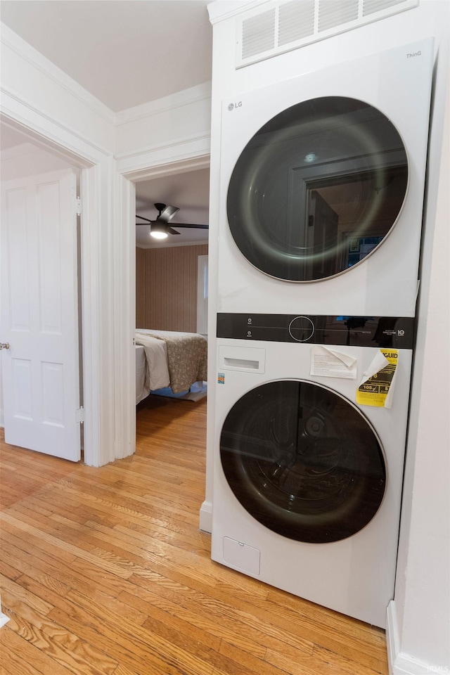 washroom with crown molding, ceiling fan, light hardwood / wood-style flooring, and stacked washing maching and dryer