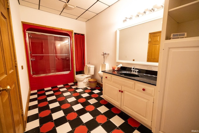 full bathroom with shower / bath combination with glass door, a drop ceiling, vanity, and toilet