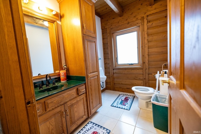 bathroom featuring beam ceiling, rustic walls, tile patterned flooring, toilet, and vanity