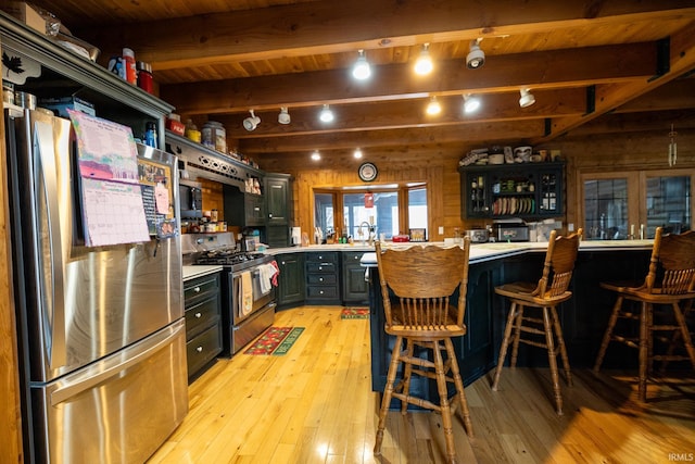 kitchen with appliances with stainless steel finishes, a kitchen breakfast bar, wooden walls, beam ceiling, and wooden ceiling