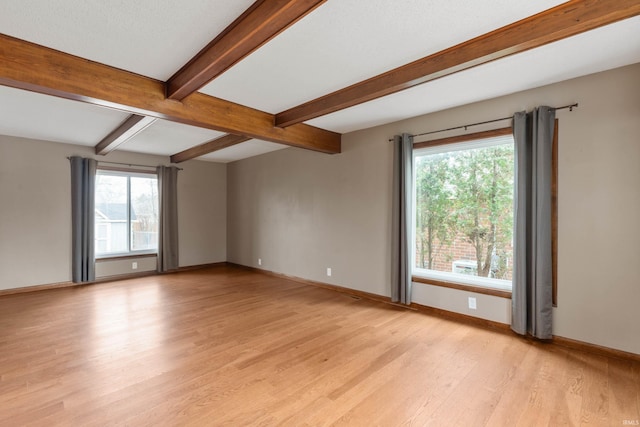 empty room with light hardwood / wood-style floors, beam ceiling, and a wealth of natural light