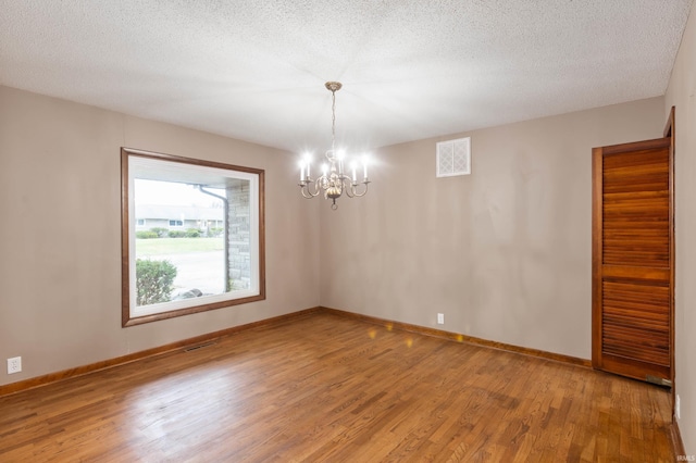 unfurnished room with hardwood / wood-style floors, a notable chandelier, and a textured ceiling