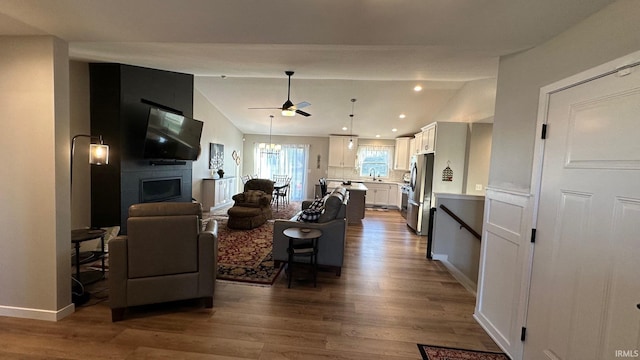 living room with sink, vaulted ceiling, hardwood / wood-style flooring, ceiling fan, and a fireplace