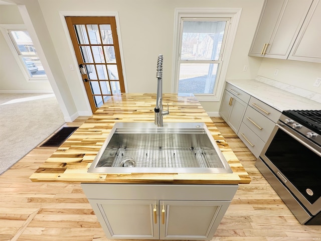 kitchen featuring butcher block countertops, stainless steel gas stove, light colored carpet, and sink