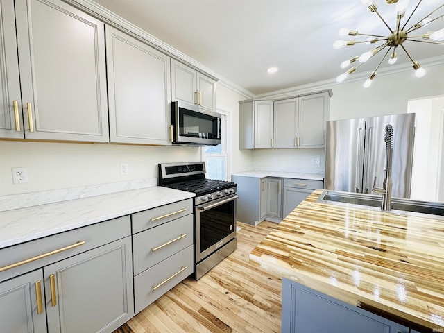 kitchen featuring gray cabinetry, crown molding, stainless steel appliances, and an inviting chandelier