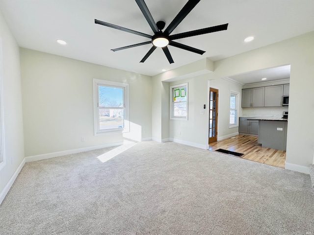 unfurnished living room featuring light carpet, a wealth of natural light, and ceiling fan