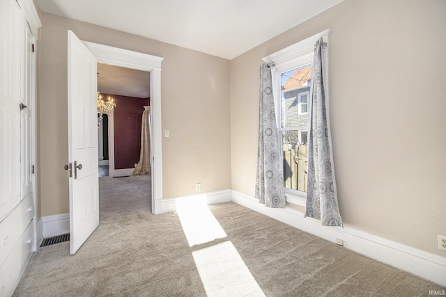 carpeted spare room with an inviting chandelier