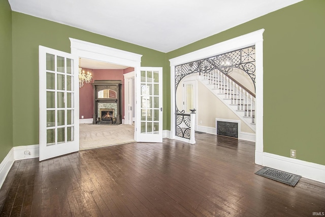 unfurnished living room with a fireplace, french doors, a chandelier, and hardwood / wood-style floors