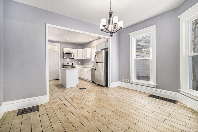 kitchen with a center island, an inviting chandelier, pendant lighting, white cabinets, and appliances with stainless steel finishes