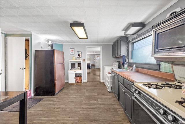 kitchen with sink, dark wood-type flooring, stove, black refrigerator, and washer and dryer