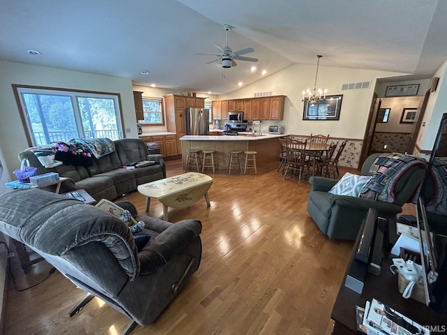 living room featuring ceiling fan with notable chandelier, light wood-type flooring, sink, and vaulted ceiling