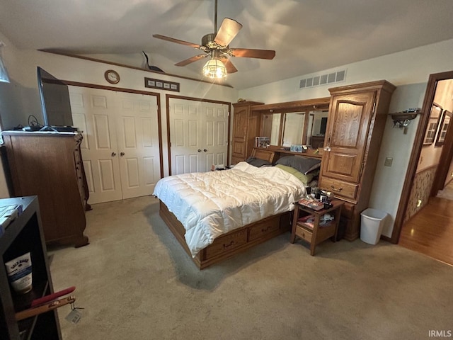 bedroom with light carpet, vaulted ceiling, ceiling fan, and multiple closets