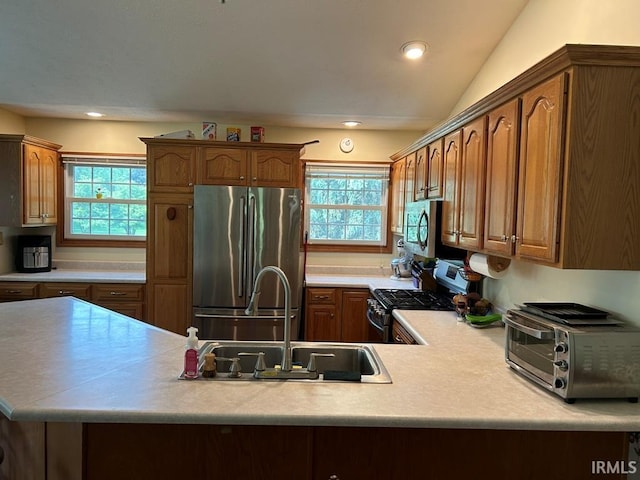 kitchen with kitchen peninsula, sink, stainless steel appliances, and lofted ceiling