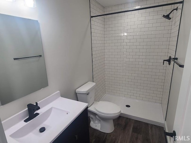 bathroom with tiled shower, vanity, hardwood / wood-style flooring, and toilet