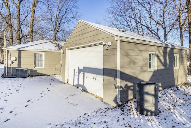 snow covered property featuring cooling unit, a garage, and an outbuilding