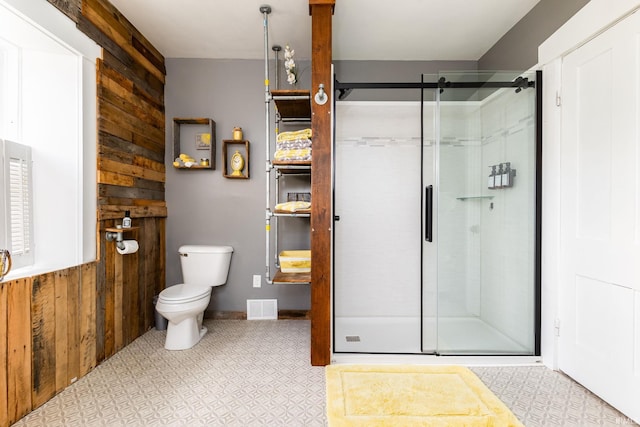 bathroom with toilet, a shower with shower door, and wood walls