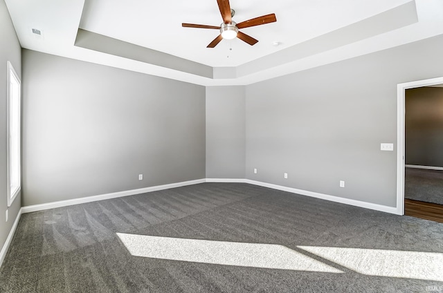 empty room featuring dark colored carpet, ceiling fan, and a raised ceiling