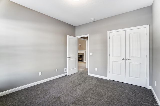 unfurnished bedroom with a fireplace, a closet, and dark colored carpet