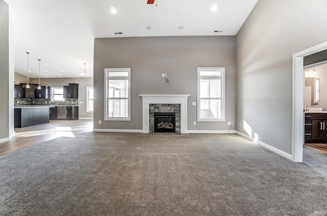 unfurnished living room with carpet flooring, a wealth of natural light, ceiling fan, and a towering ceiling