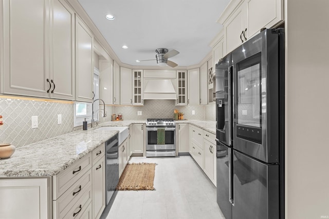 kitchen with light stone countertops, sink, stainless steel appliances, white cabinets, and custom range hood