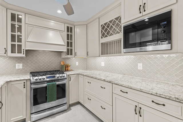 kitchen featuring custom exhaust hood, decorative backsplash, built in microwave, light stone counters, and stainless steel range with gas stovetop