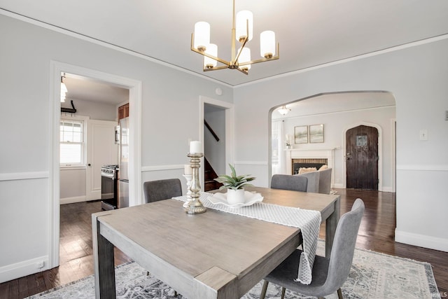 dining area with crown molding, a chandelier, dark hardwood / wood-style floors, and a brick fireplace