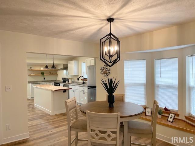 dining area featuring a textured ceiling, a notable chandelier, light wood-type flooring, and sink