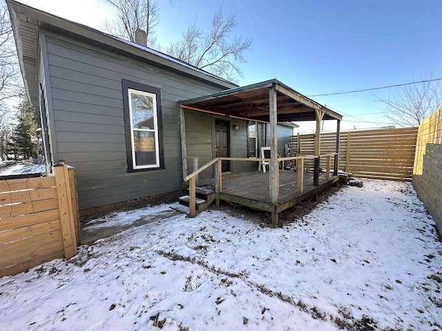 snow covered rear of property with a deck and a fenced backyard