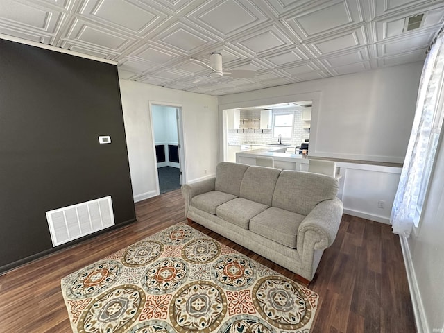 living room featuring an ornate ceiling, dark wood finished floors, visible vents, and baseboards