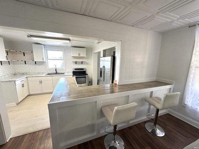 kitchen with stainless steel appliances, decorative backsplash, white cabinetry, a sink, and a peninsula