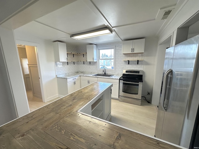 kitchen with a sink, stainless steel appliances, open shelves, and white cabinets