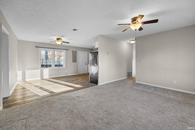 unfurnished living room featuring ceiling fan, carpet floors, a textured ceiling, and electric panel