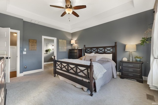 carpeted bedroom with a tray ceiling, connected bathroom, and ceiling fan