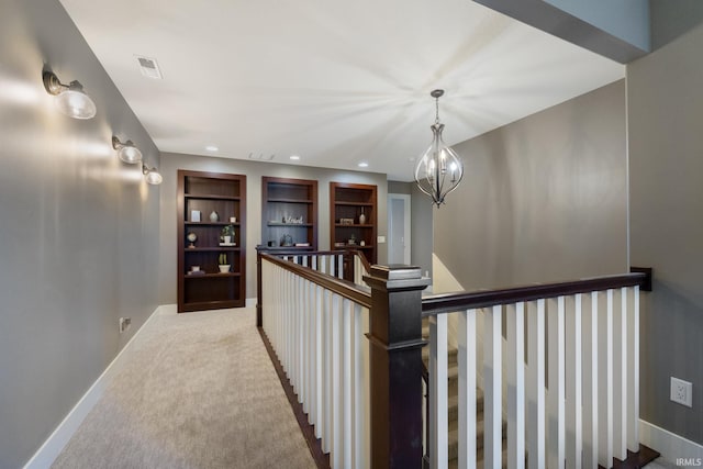 corridor with built in shelves, light colored carpet, and an inviting chandelier