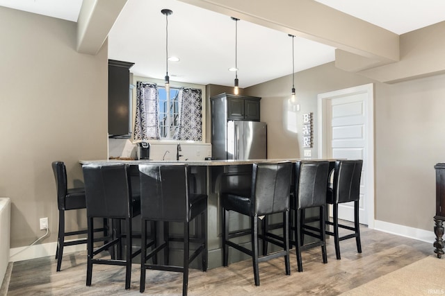 kitchen featuring a kitchen bar, kitchen peninsula, light wood-type flooring, decorative light fixtures, and stainless steel refrigerator