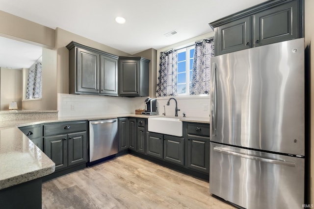 kitchen with backsplash, sink, appliances with stainless steel finishes, light hardwood / wood-style floors, and light stone counters