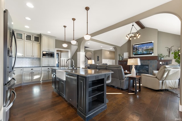 kitchen with backsplash, a center island with sink, lofted ceiling with beams, a fireplace, and stainless steel appliances