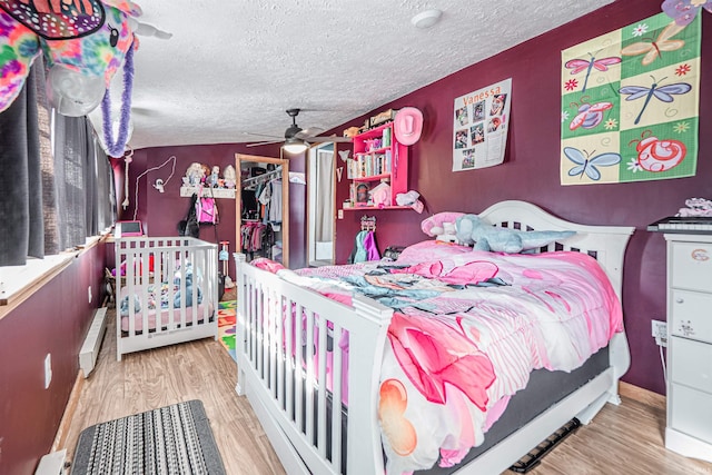 bedroom featuring ceiling fan, a baseboard radiator, light hardwood / wood-style floors, a textured ceiling, and a closet