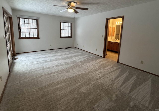 unfurnished bedroom with sink, ensuite bath, ceiling fan, a textured ceiling, and light colored carpet