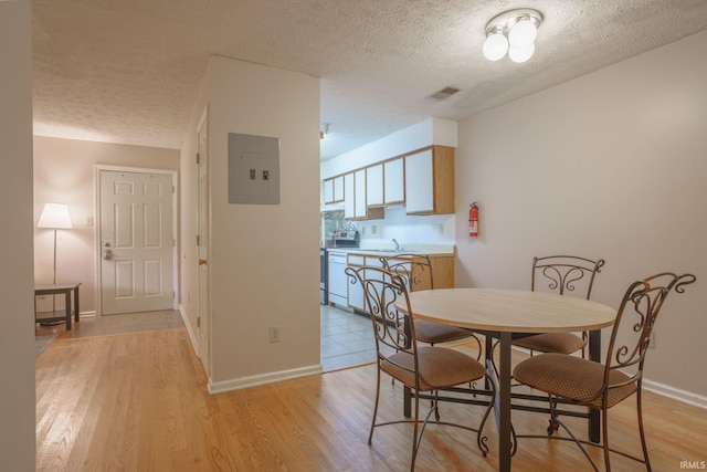 dining space featuring electric panel, light hardwood / wood-style floors, and a textured ceiling