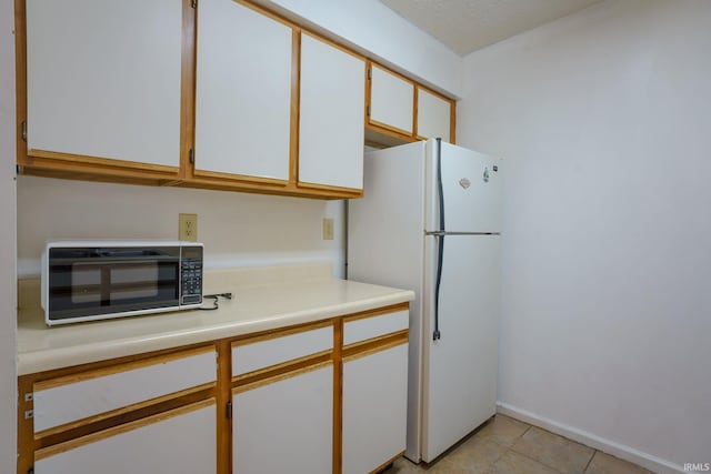 kitchen featuring white cabinets, white refrigerator, and light tile patterned floors