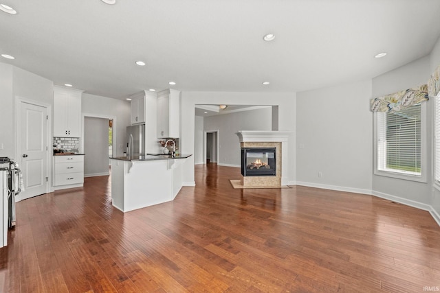 unfurnished living room with a multi sided fireplace, sink, and dark wood-type flooring