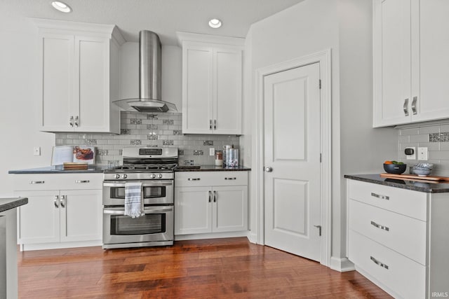 kitchen featuring range with two ovens, wall chimney exhaust hood, dark hardwood / wood-style floors, decorative backsplash, and white cabinetry