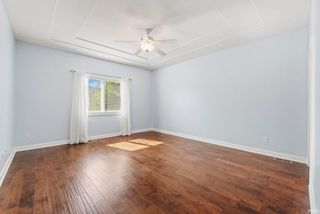 unfurnished room with ceiling fan, dark wood-type flooring, and a tray ceiling